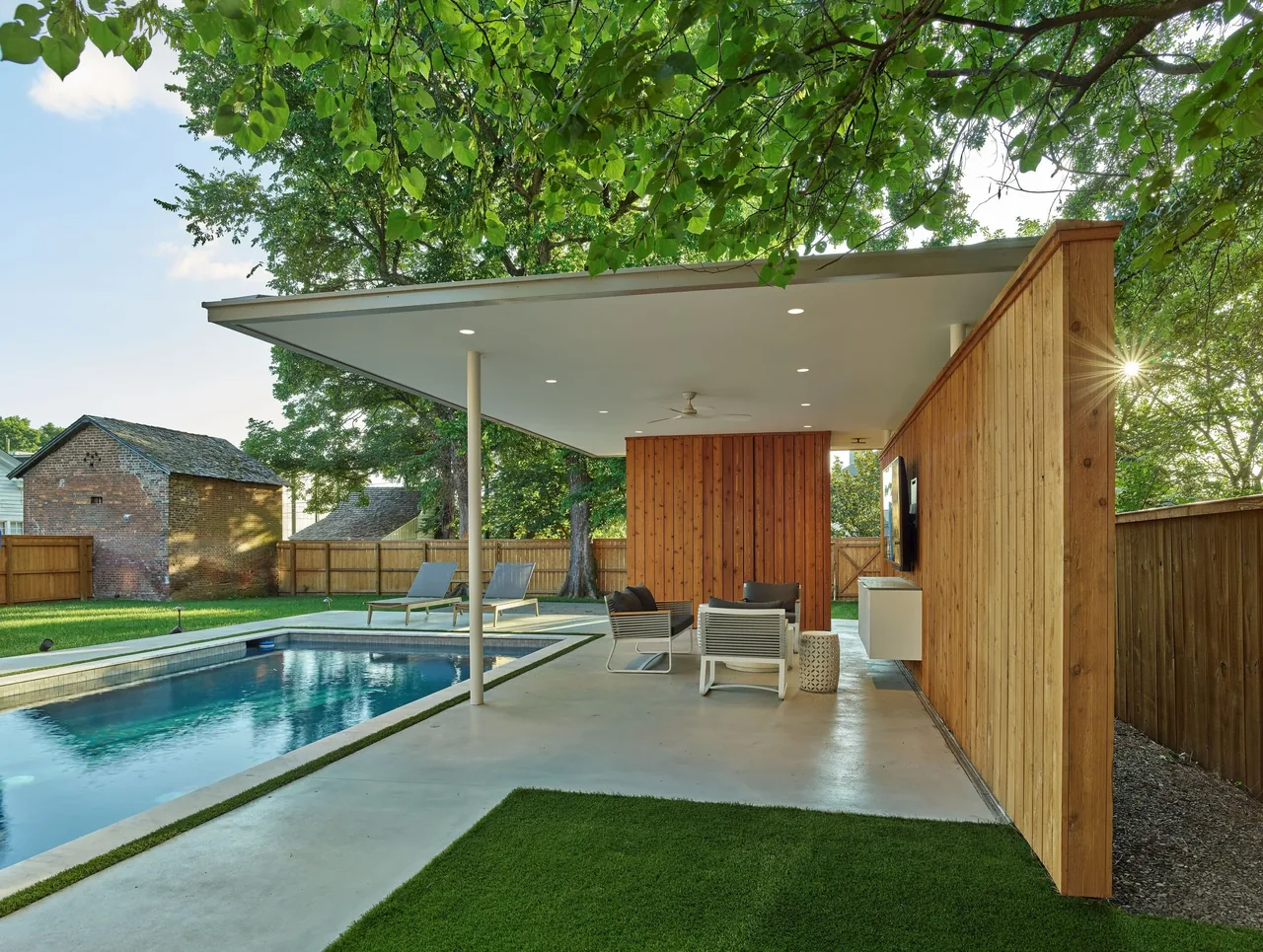 The Werner Pool & Pavilion features a wood privacy wall, covered patio seating, and an outdoor TV next to a rectangular pool.