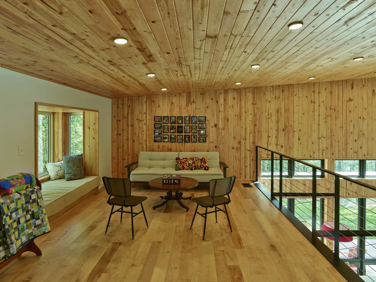 Living room with wood plank ceiling and walls, hardwood floor, metal railing overlooking a lower level, and built-in window seating.