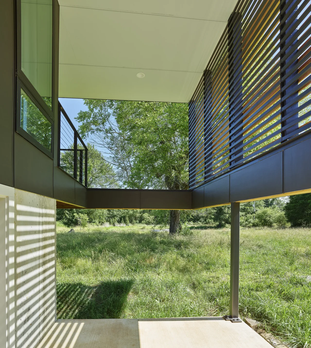 Covered patio area with cable railing, wood slat screening, and concrete flooring at Willis Residence by deMx Architecture.