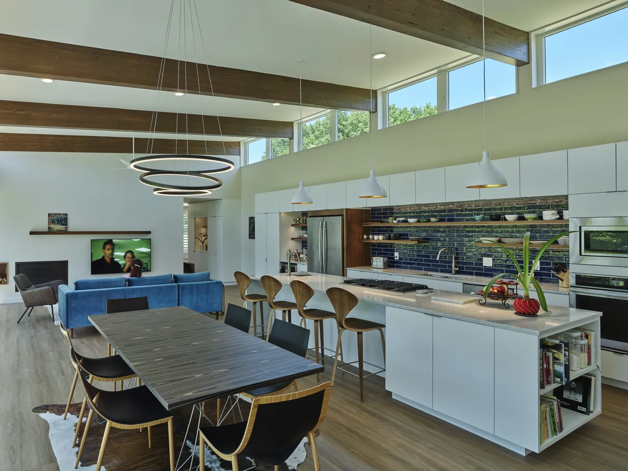 Open kitchen and dining space features high clerestory windows, wood beams, and blue tile backsplash at Willis Residence by deMx Architecture.
