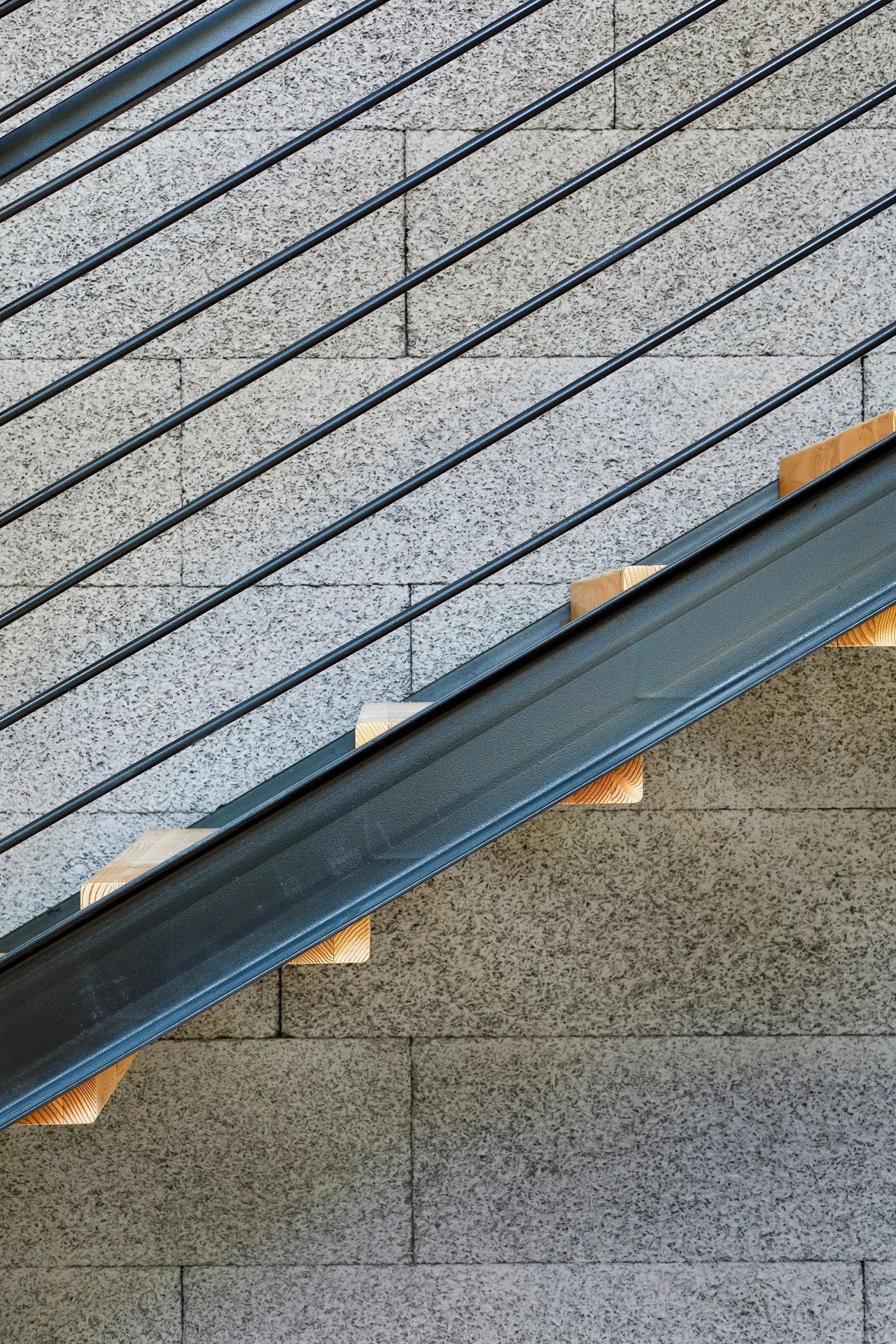Modern staircase detail with textured concrete block wall and black metal railings at Jesse Street House.