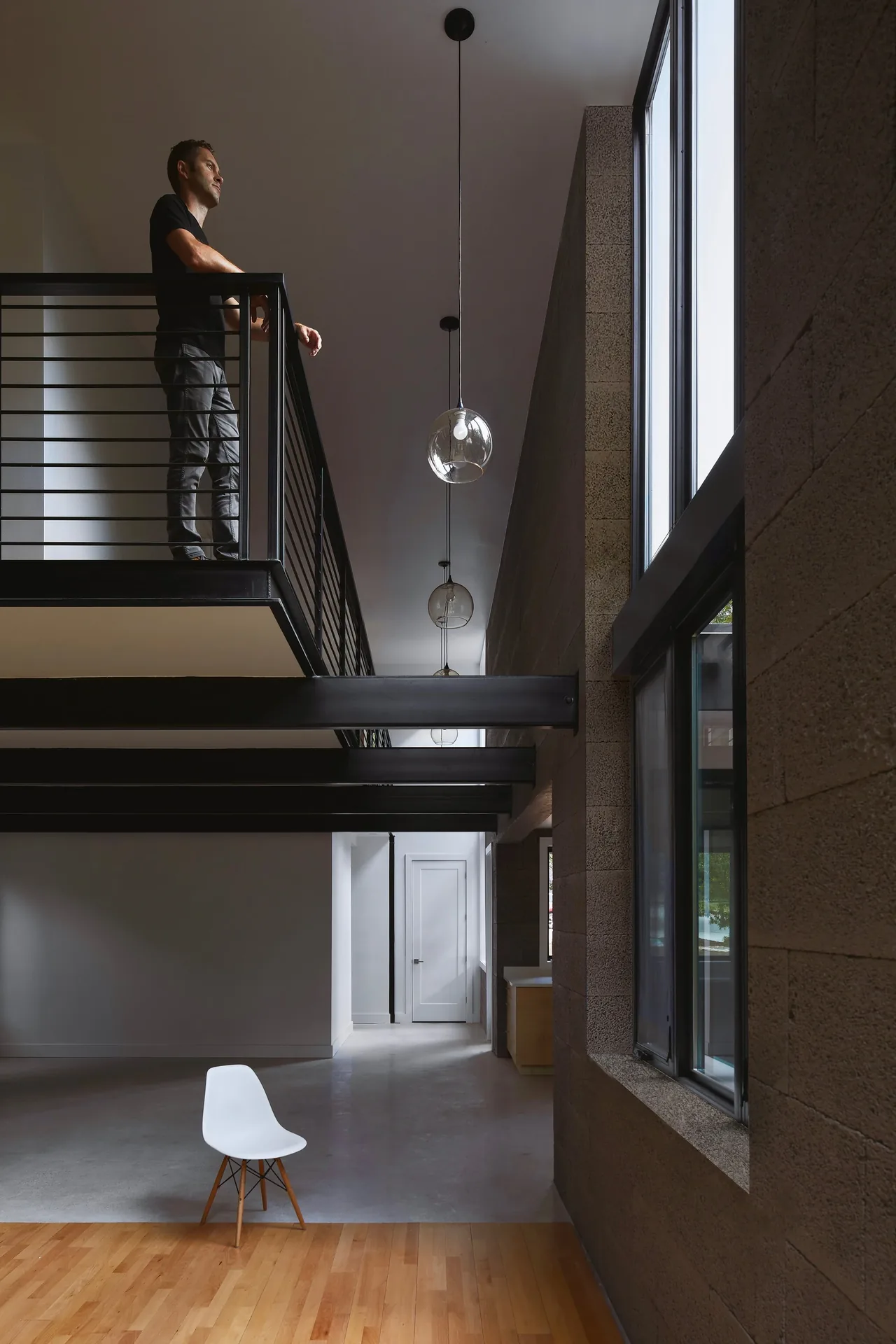 The Jesse Street House features a two-story interior with textured concrete block walls and black metal railings allowing views through large windows.