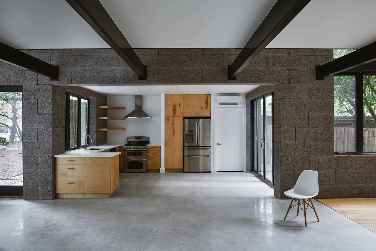 Open kitchen with natural wood cabinetry and concrete floors features large windows with black frames and exposed ceiling beams.