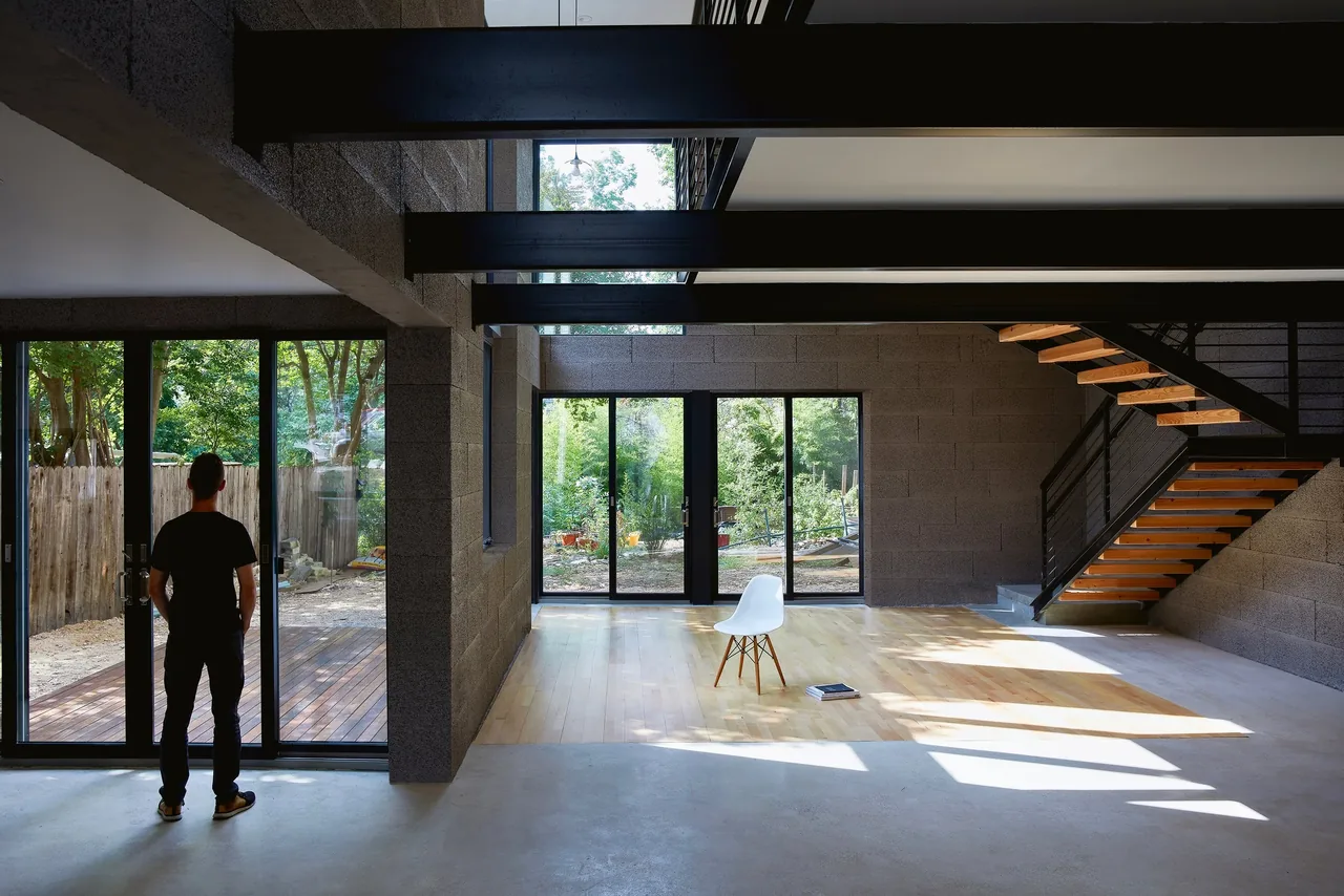The Jesse Street House interior features concrete block walls, large black-framed sliding glass doors, and a wood and metal open riser staircase.