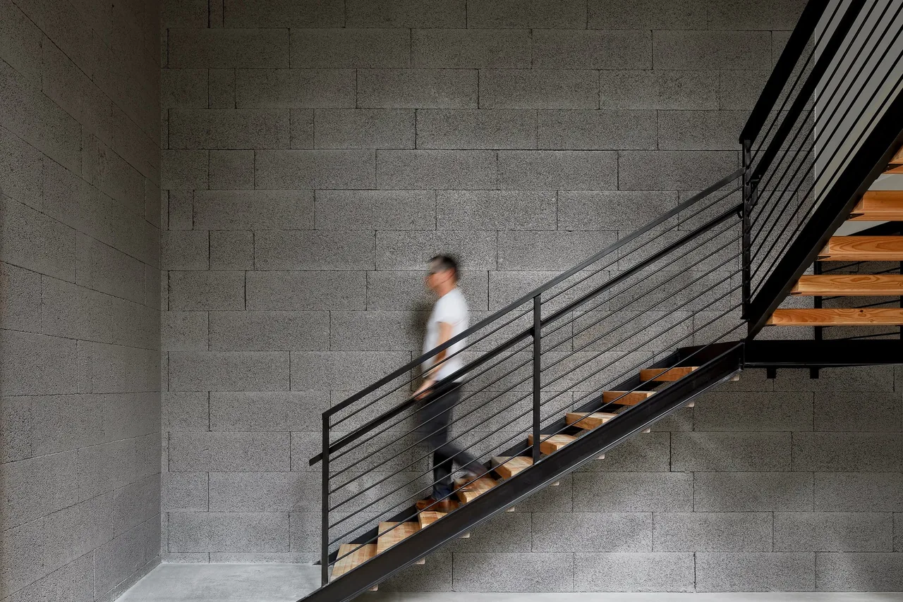 Floating stairs with wooden treads and metal railings inside a home with textured concrete block walls.