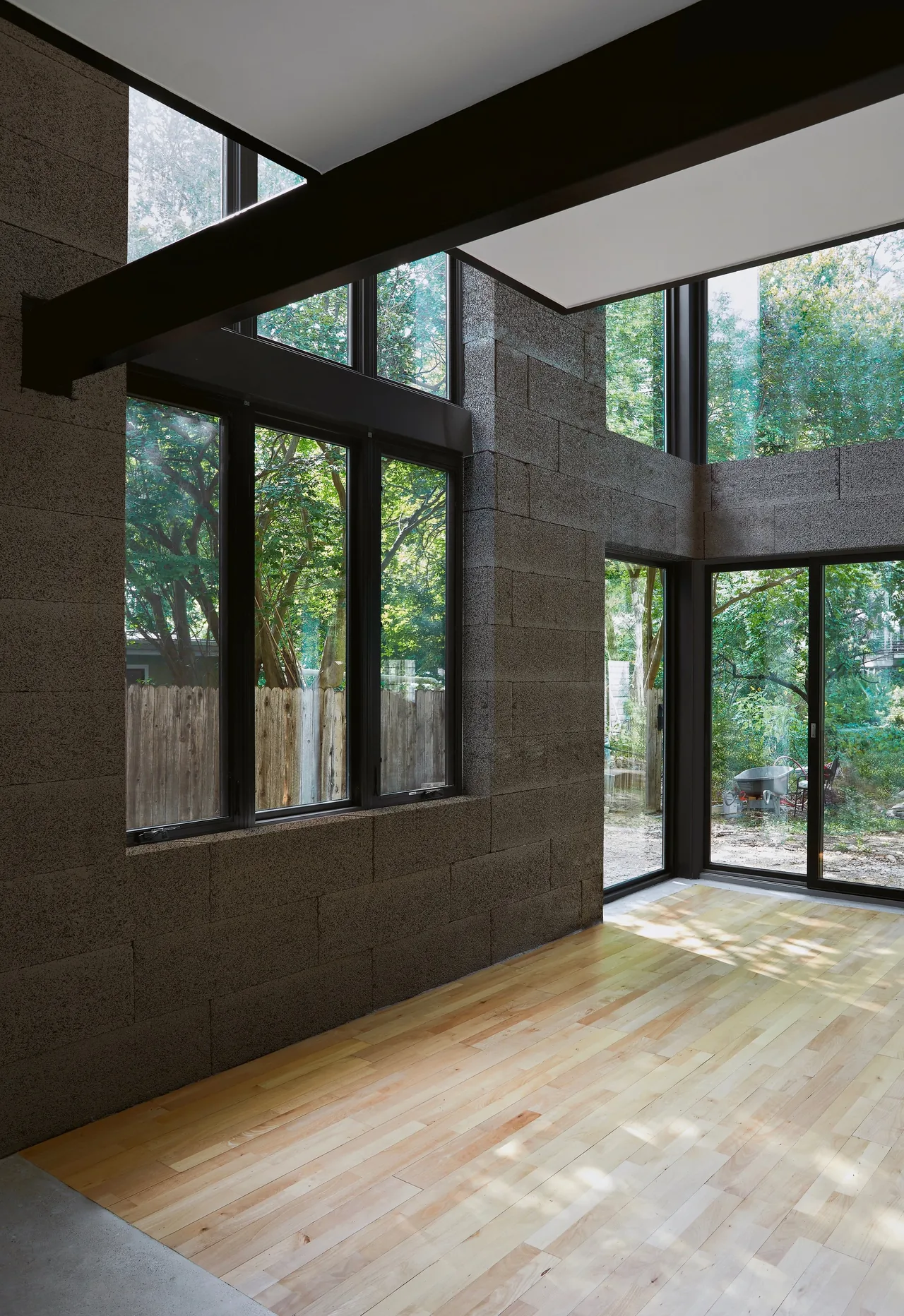 Room interior features two-story concrete block walls with black window frames and large windows looking out to greenery.
