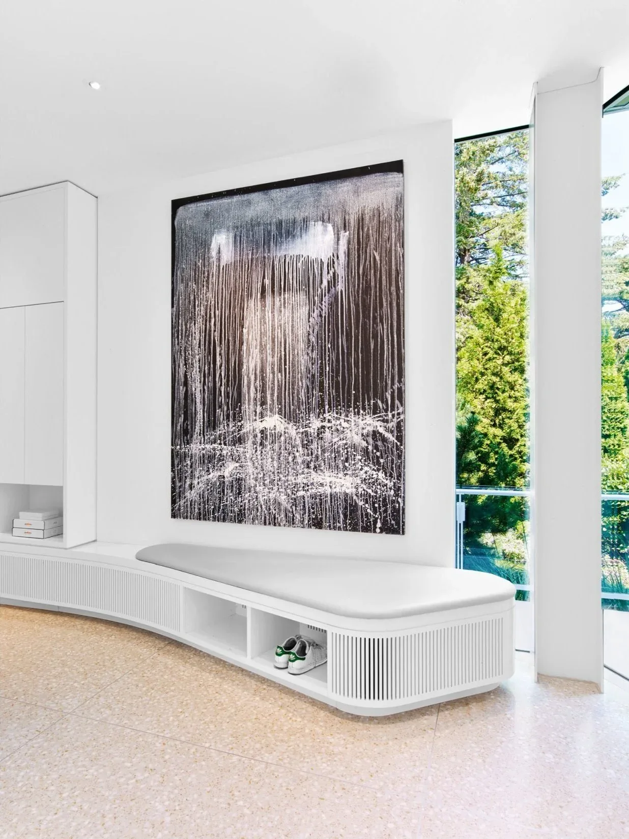Curved bench seating with storage beneath a large black and white abstract painting beside tall windows.