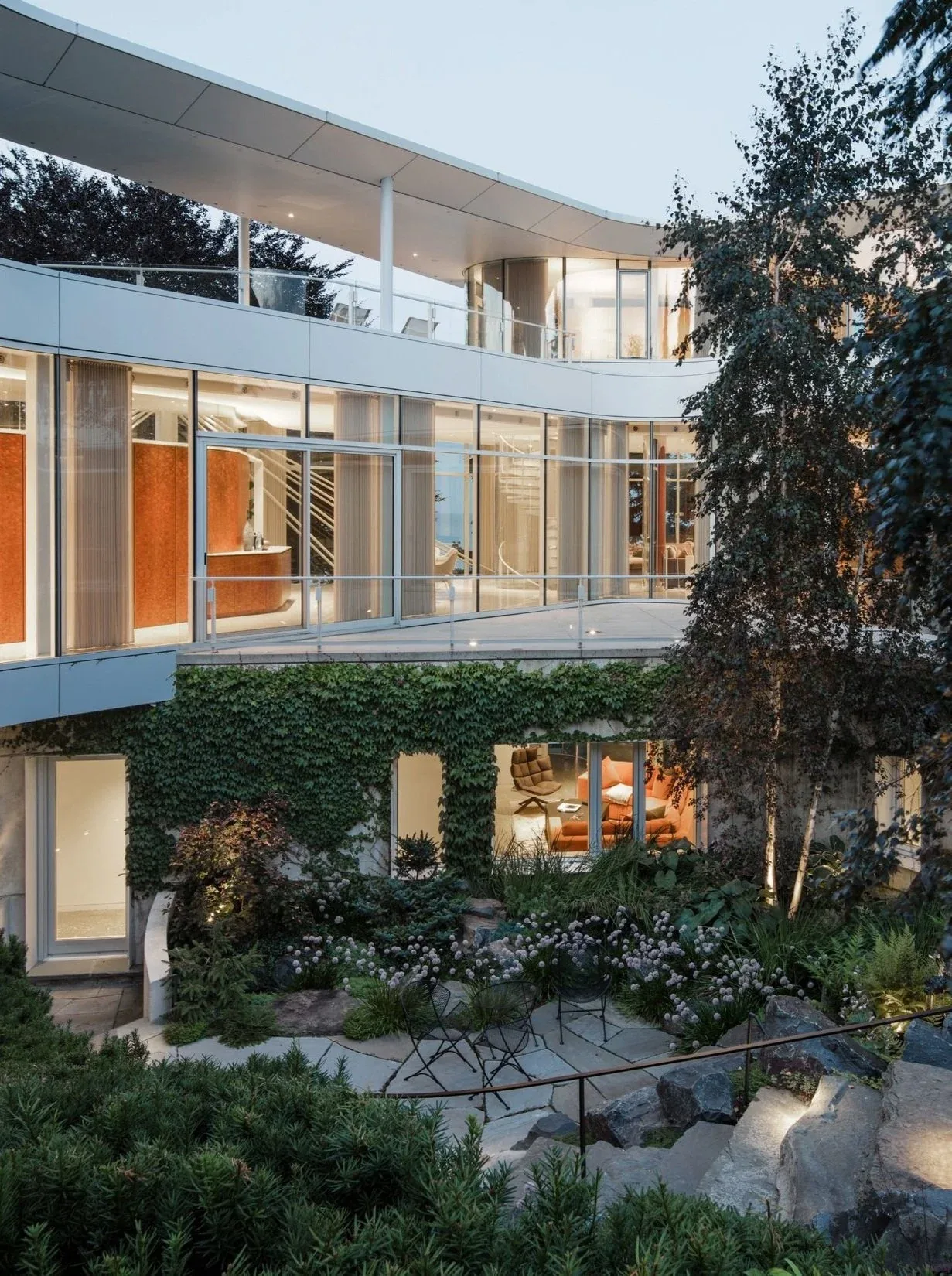 Lake Michigan Residence features floor-to-ceiling glazing and an ivy-covered exterior with landscaped garden seating areas.