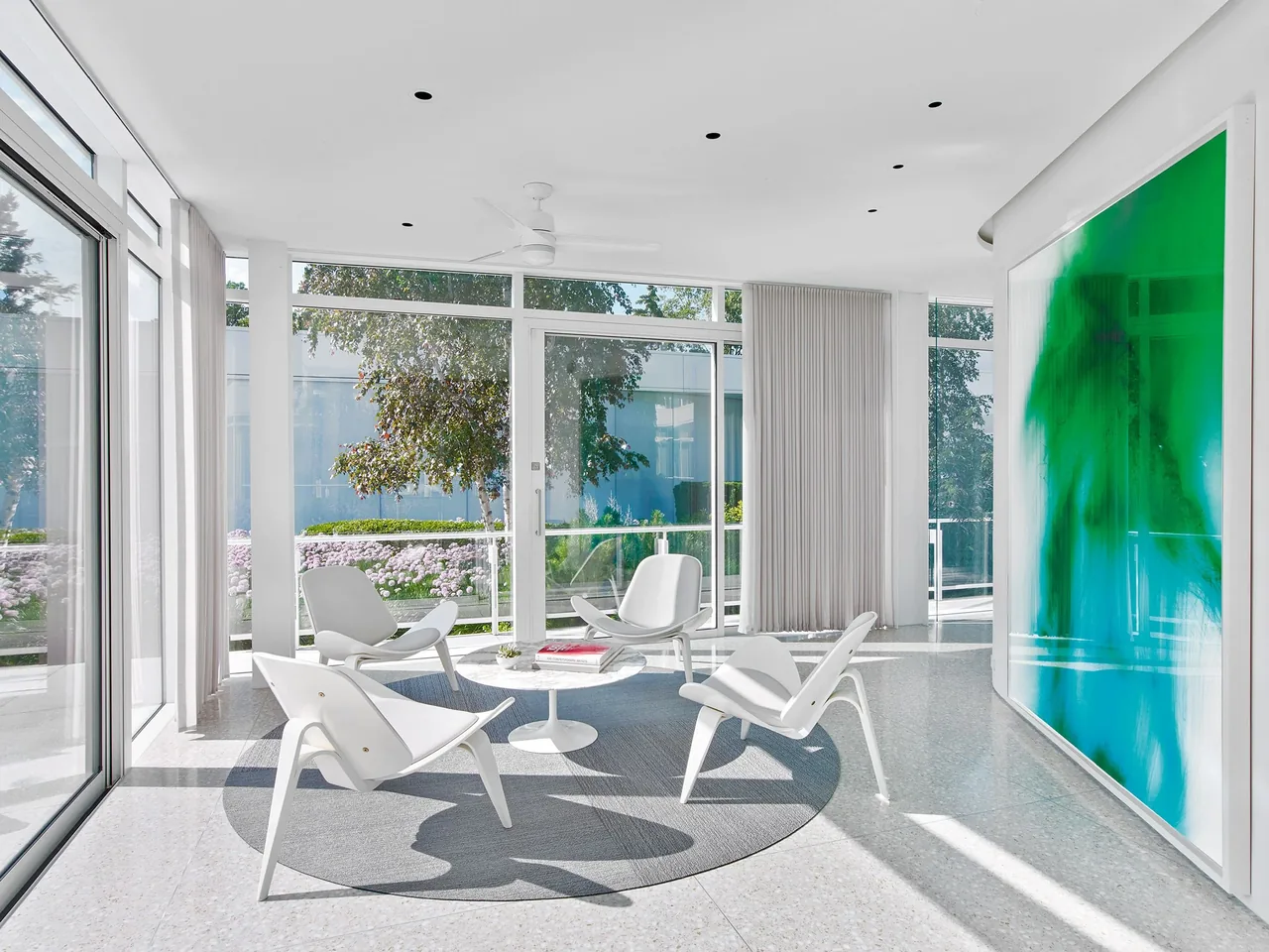 The Lake Michigan Residence living area features floor-to-ceiling glazing with white modern chairs around a small table on a circular rug.