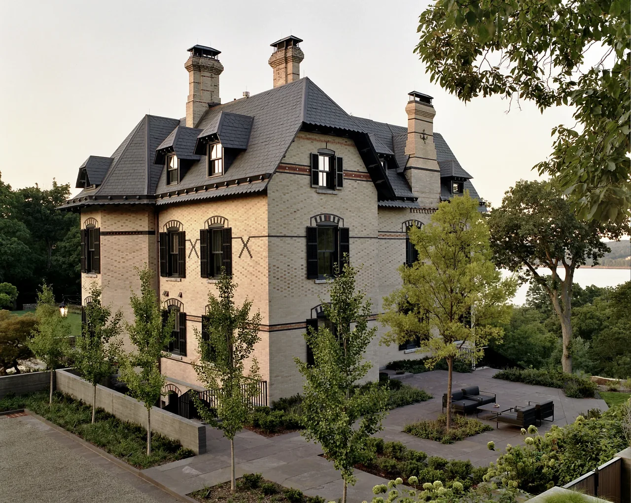 The Neiderhurst Estate features brick construction with a slate roof and multiple chimneys, accompanied by an outdoor seating patio.