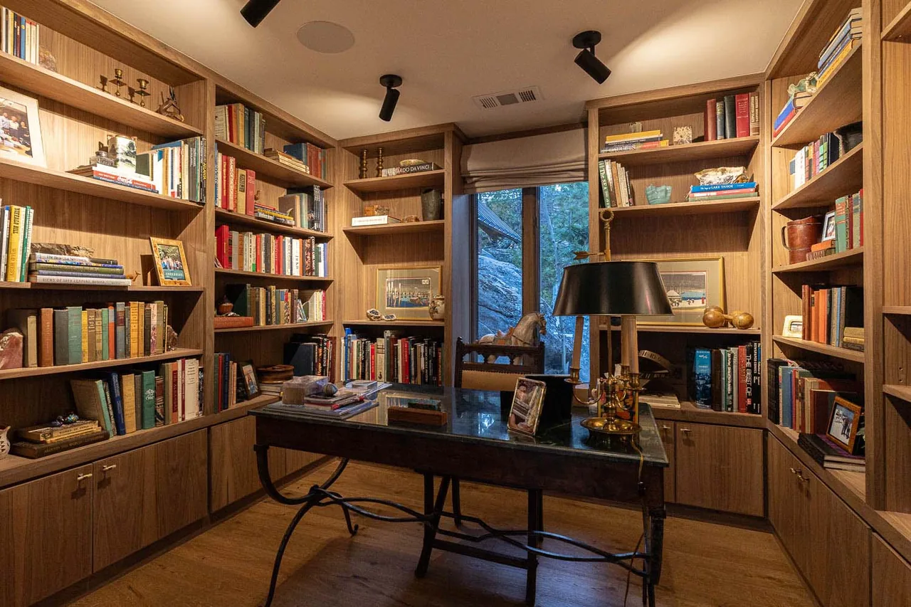 Interior view of a study with wood-paneled built-in bookshelves and a window overlooking natural landscape.