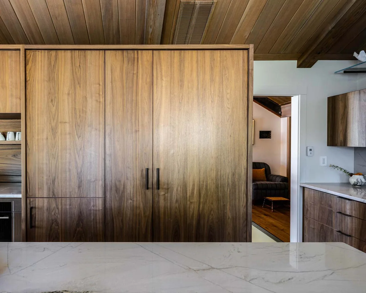 Large wooden cabinetry and a marble countertyop are visible in the kitchen with a glimpse into a cozy living room beyond.