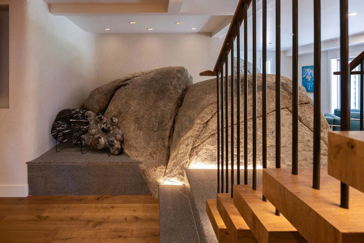 A wooden staircase with black metal railings contrasts with a large stone feature integrated into the interior design at Bold Tahoe Lodge Transformation.