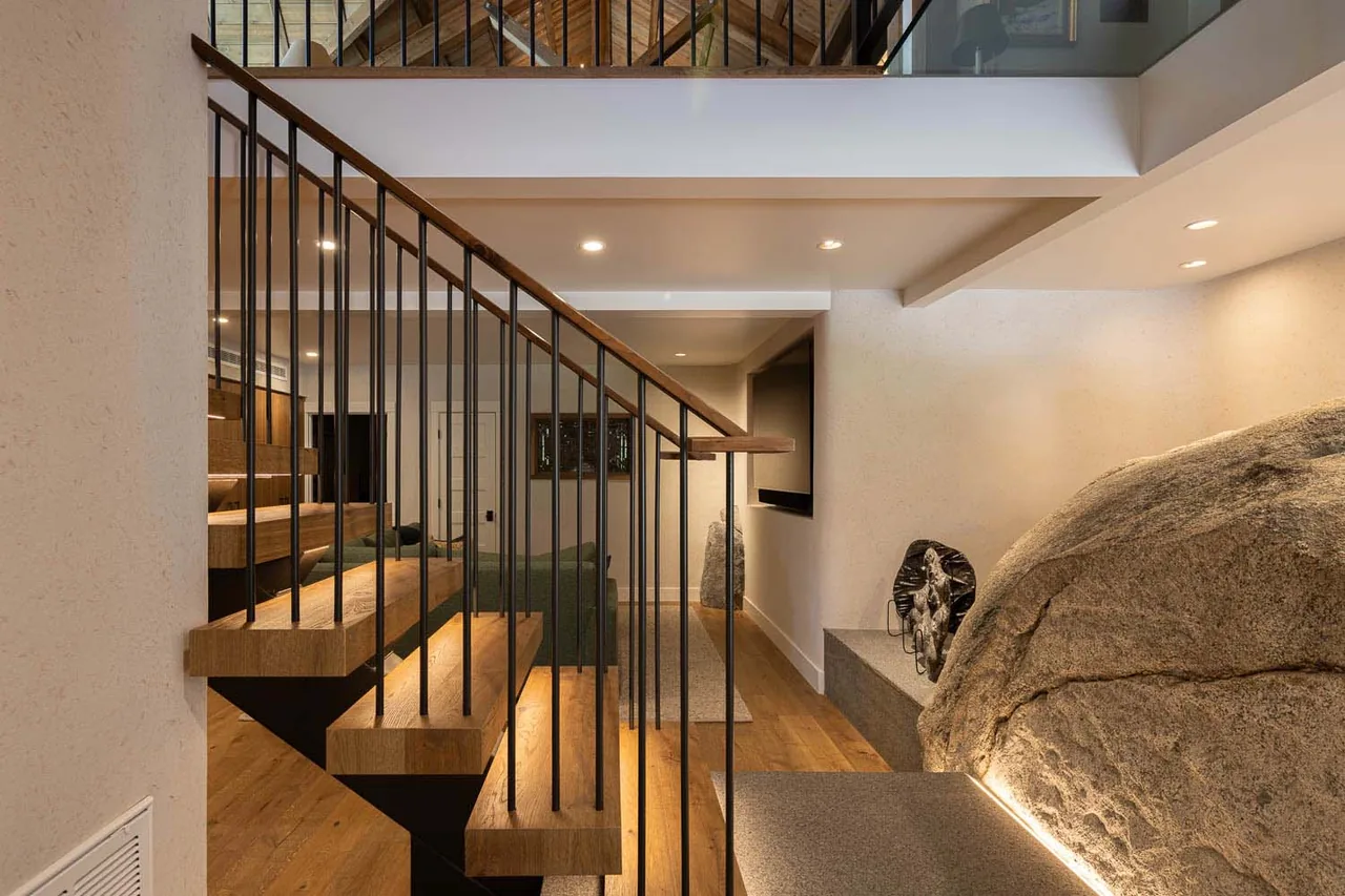 Bold Tahoe Lodge interior shows a staircase with wood steps and metal spindles next to a large natural rock feature with under-stair lighting.