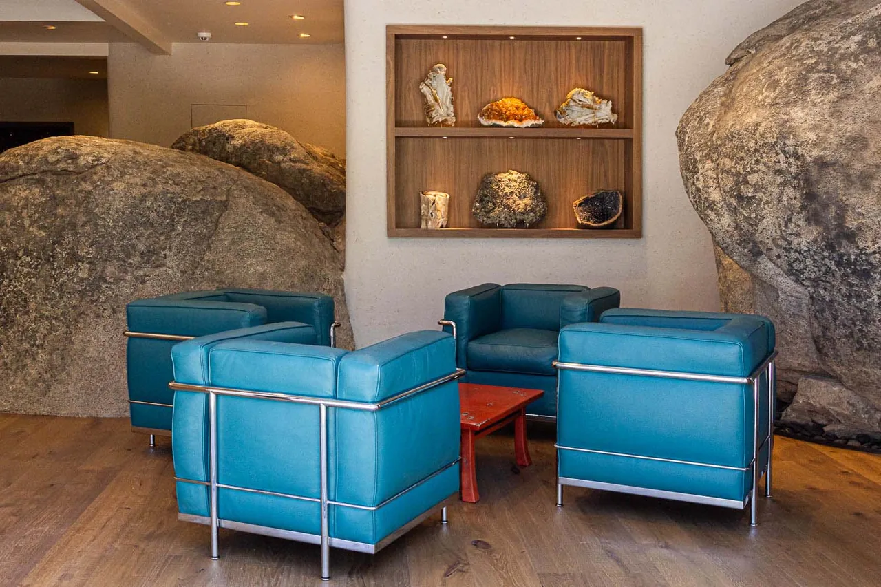 Seating area with blue leather armchairs framed by natural rock features and a built-in wooden shelf displaying mineral specimens.