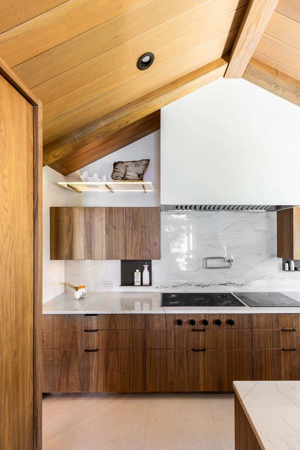 Kitchen features walnut cabinetry, vaulted wood ceiling, and marble backsplash with integrated cooktop and vent hood.