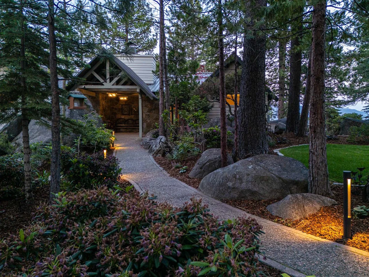 The lodge features a stone exterior and a gable roof with illuminated pathway lighting through the surrounding forest.