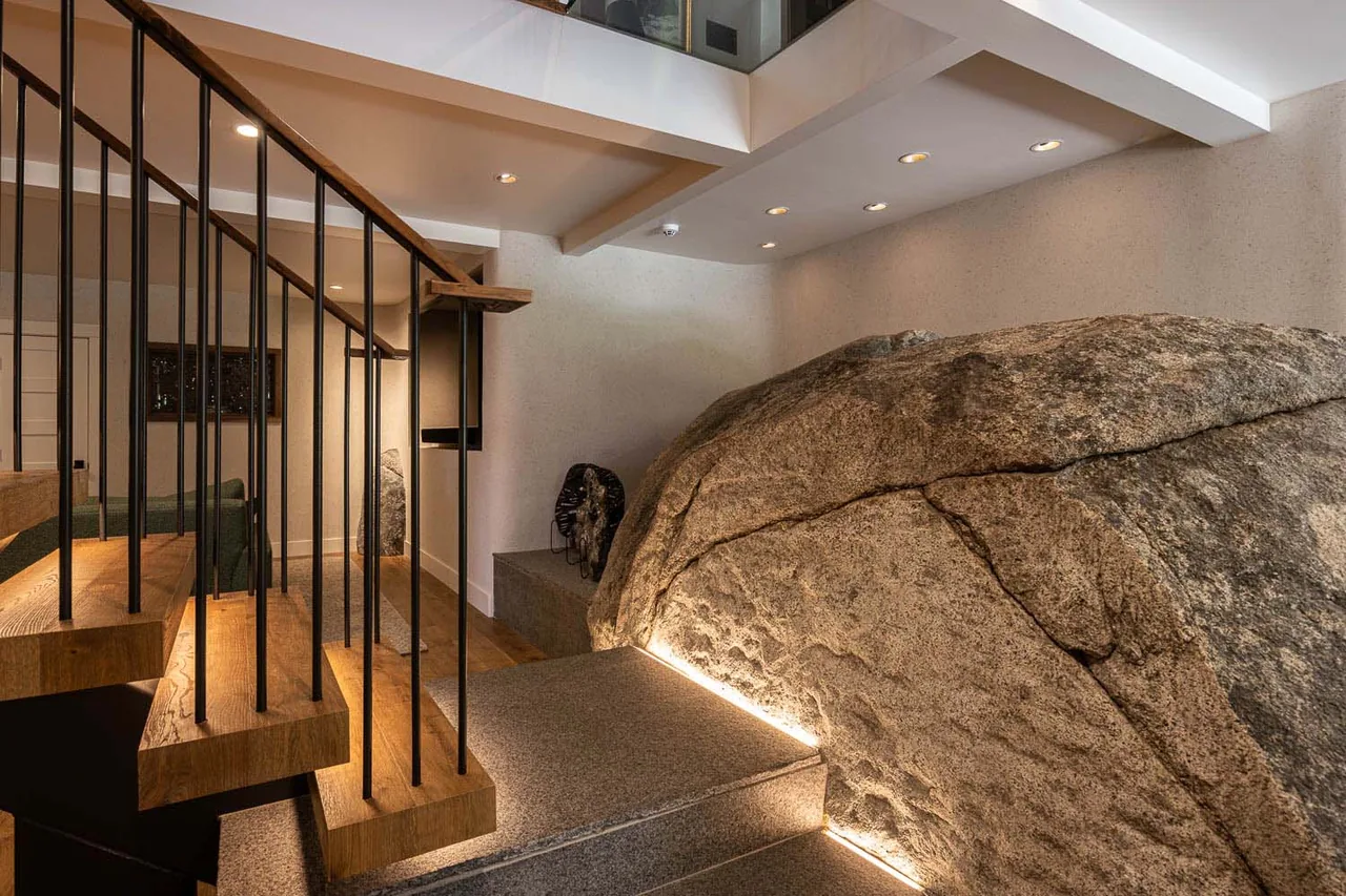 Interior stair design featuring a suspended wood staircase with metal balusters next to a large natural rock feature with integrated lighting.