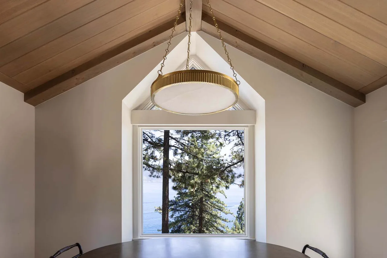 Dining space features a vaulted wood ceiling and a large window with a view of pine trees and water.