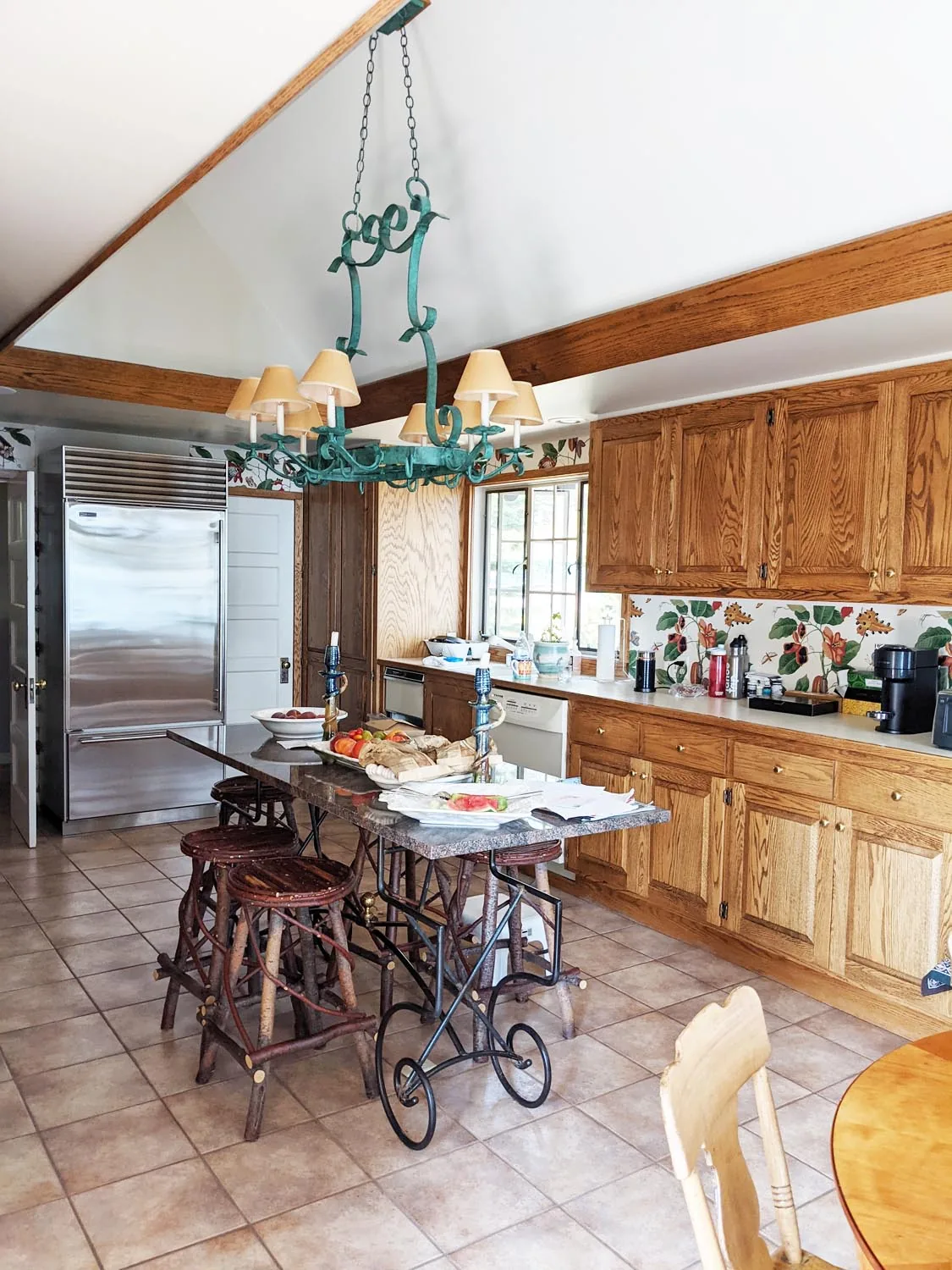 Kitchen featuring wooden cabinetry, tile flooring, a stainless steel refrigerator, and a wrought iron island with wood stools.