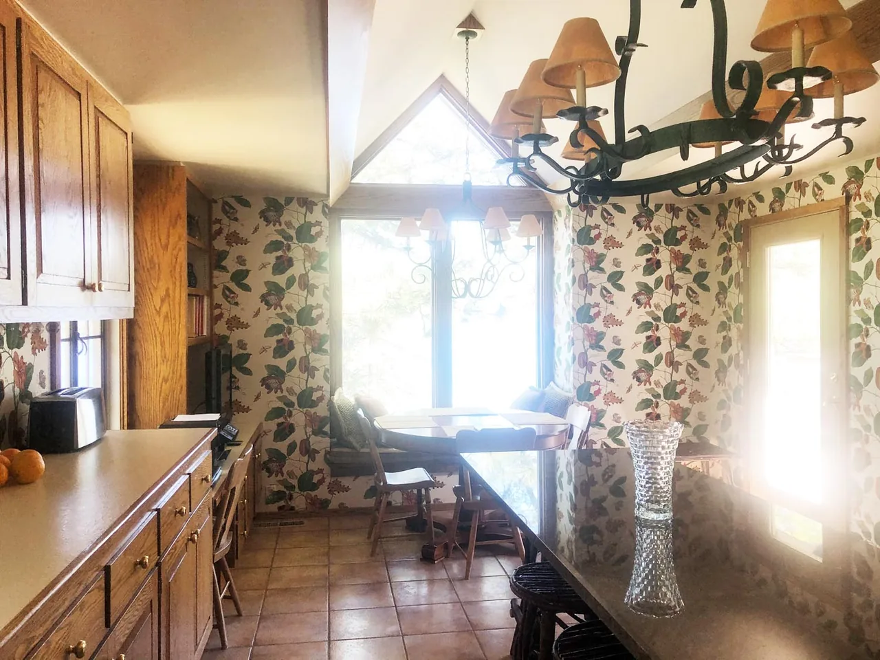 Kitchen and dining nook with floral wallpaper, wooden cabinets, and a chandelier under a vaulted ceiling with timber trusses.