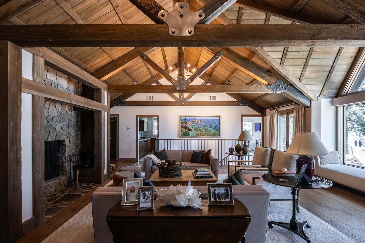 Living room featuring a wood vaulted ceiling with exposed beams and a stone fireplace, overlooking an outdoor view through large windows.