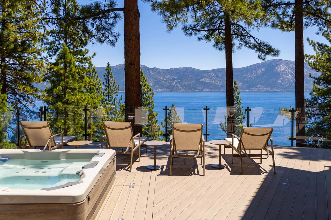 Deck area with loungers and a hot tub offers a lake view surrounded by forested mountains.