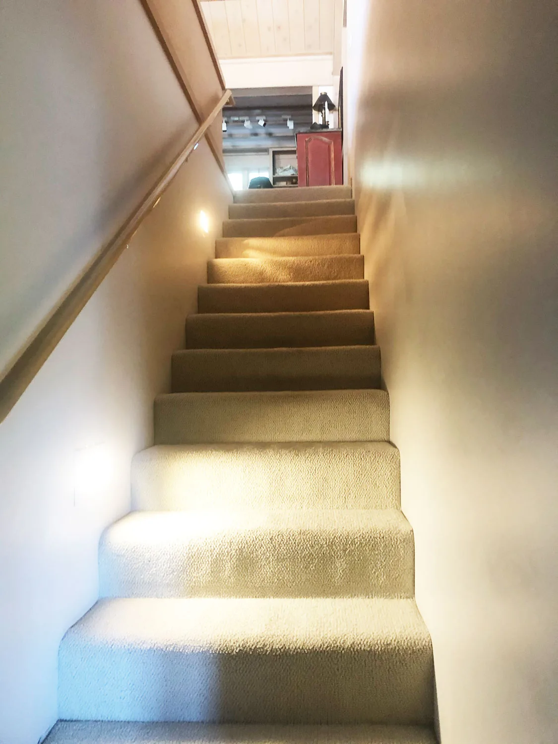 Carpeted staircase with wood handrail leading to an upper landing with visible furniture.