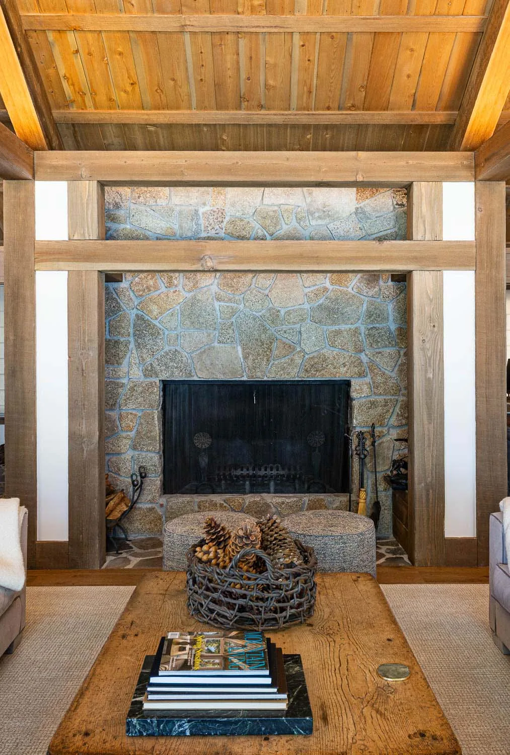 Stone hearth with exposed wood beams in a living room featuring a rustic coffee table.
