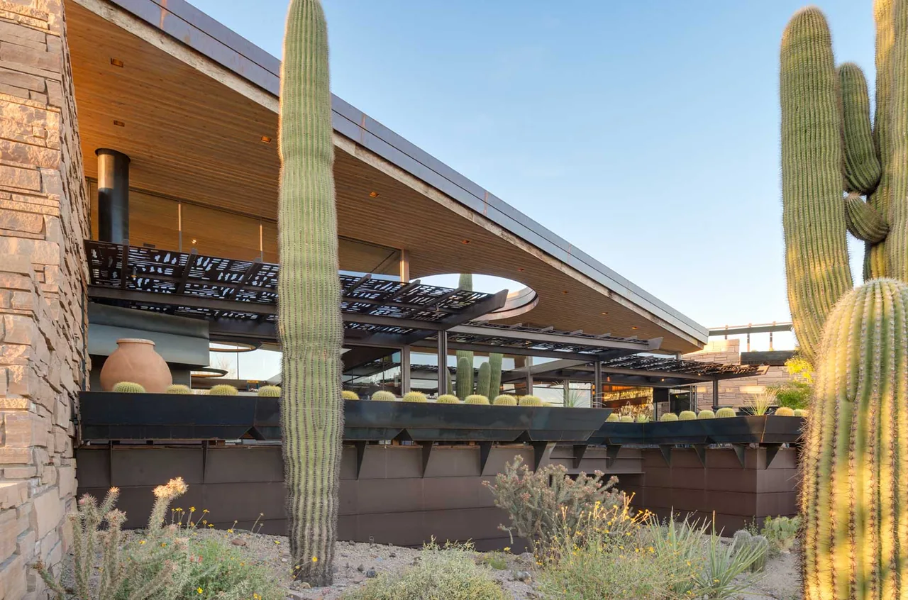 Saguaro Ridge features a sloped roof and stone exterior with desert landscaping including tall cacti.
