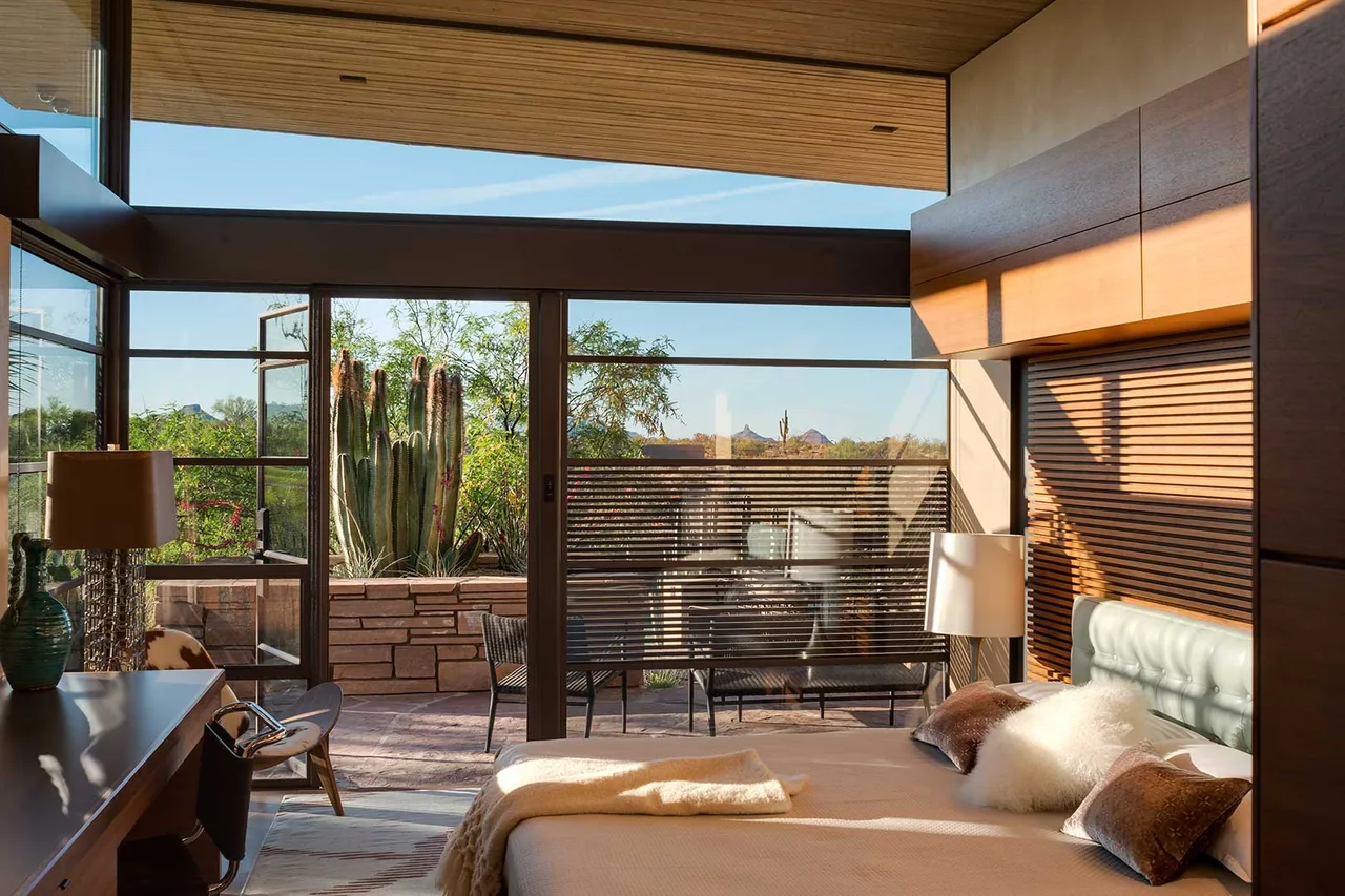 Saguaro Ridge bedroom features floor-to-ceiling glazing facing a stone-wall patio with desert landscaping.