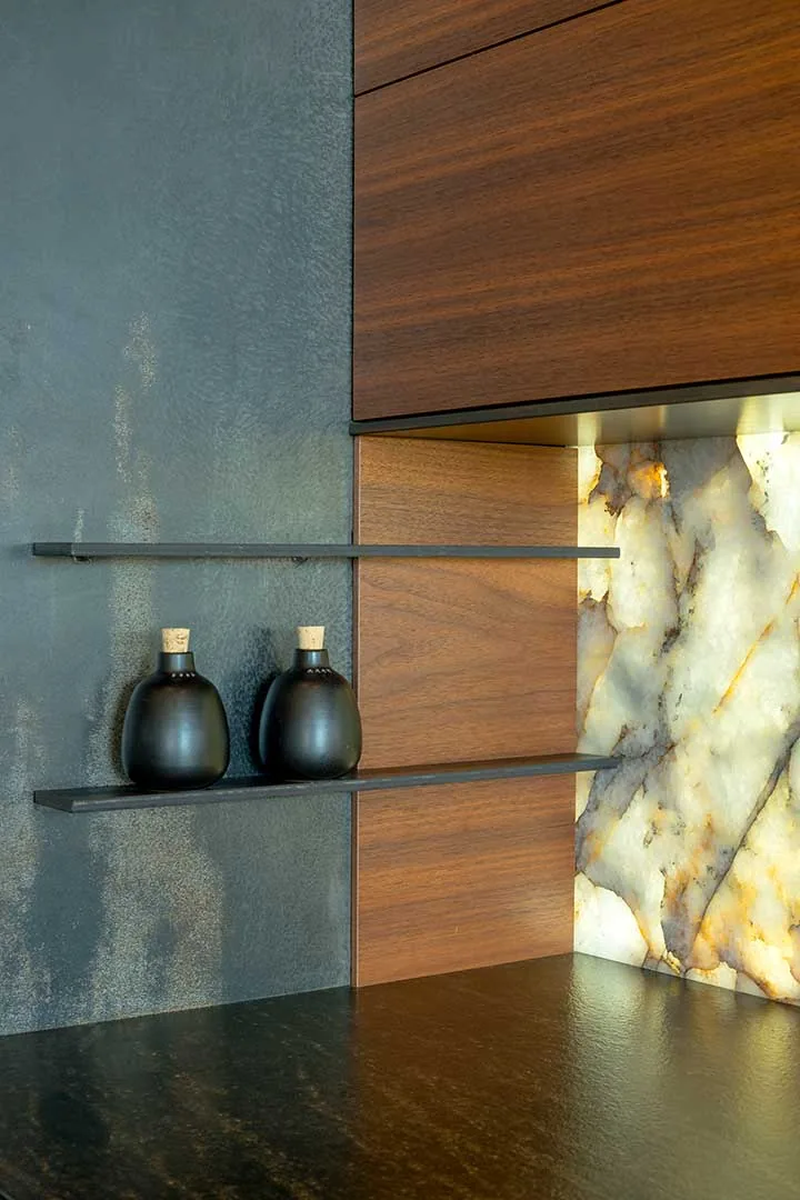 Two black ceramic bottles with cork tops sit on floating metal shelves, complemented by wood paneling and illuminated stone wall