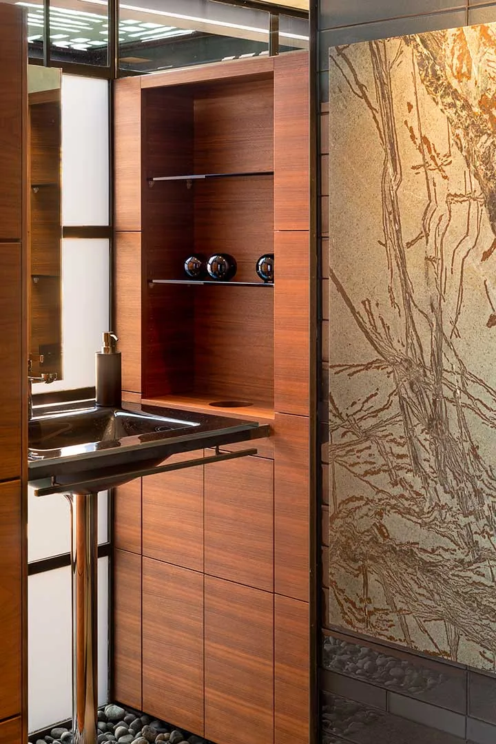 Bathroom corner featuring wood cabinets, a black undermount sink, and a decorative stone wall panel at Saguaro Ridge.
