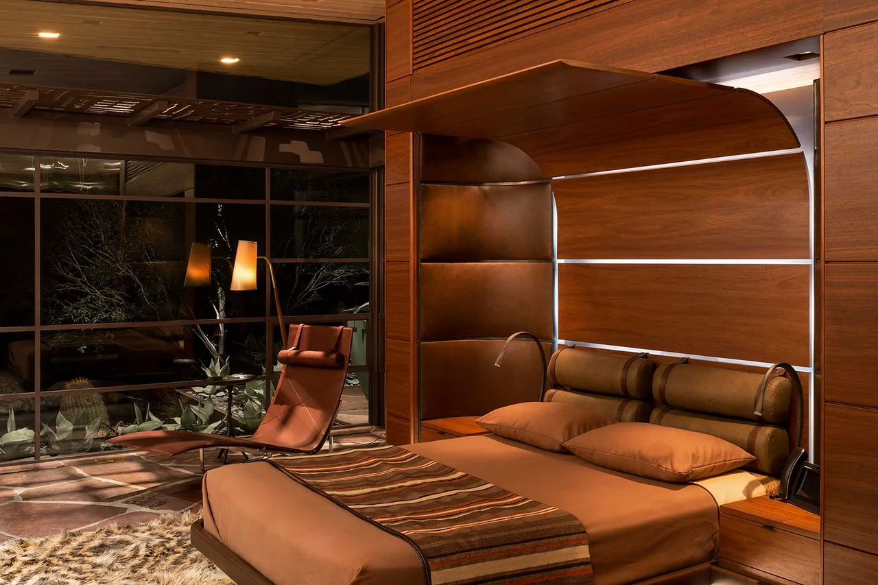 The Saguaro Ridge bedroom features warm wood paneling, patterned textiles, and a leather lounge chair beside floor-to-ceiling windows.
