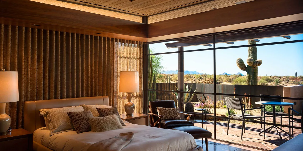 The Saguaro Ridge bedroom features floor-to-ceiling glazing with a view of a desert landscape and patio seating.