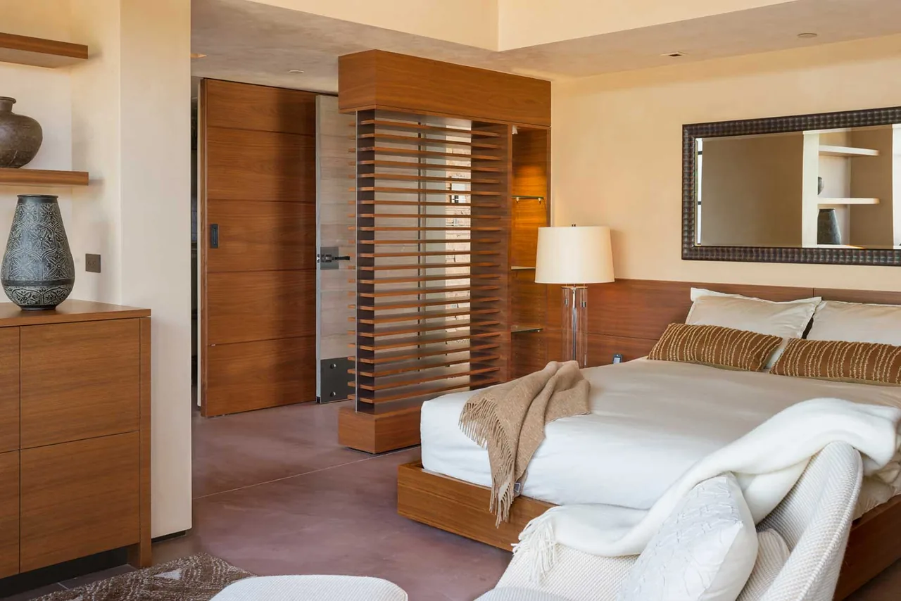 Saguaro Ridge bedroom features warm wood tones, a wooden slat divider, and neutral textiles by Douglas Fredrikson Architects.