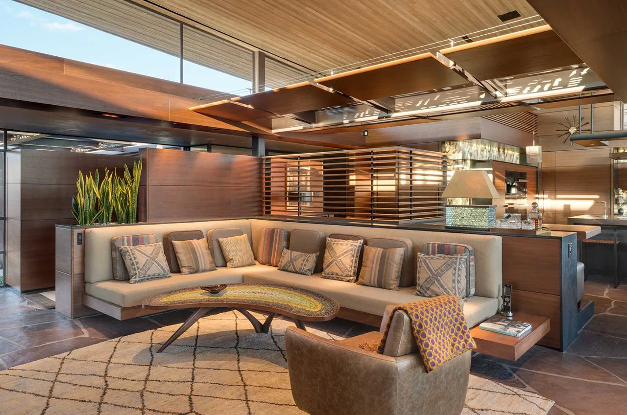 Living room features a curved built-in bench sofa, striped cushions, and a stone tile floor under a wood-paneled ceiling with suspended panels.