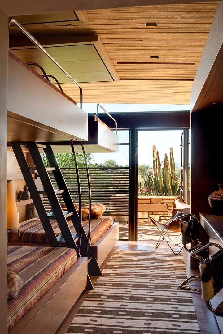 Cozy bunk bed room with wood ceiling, striped cushions, and access to an outdoor patio featuring cactus plants.