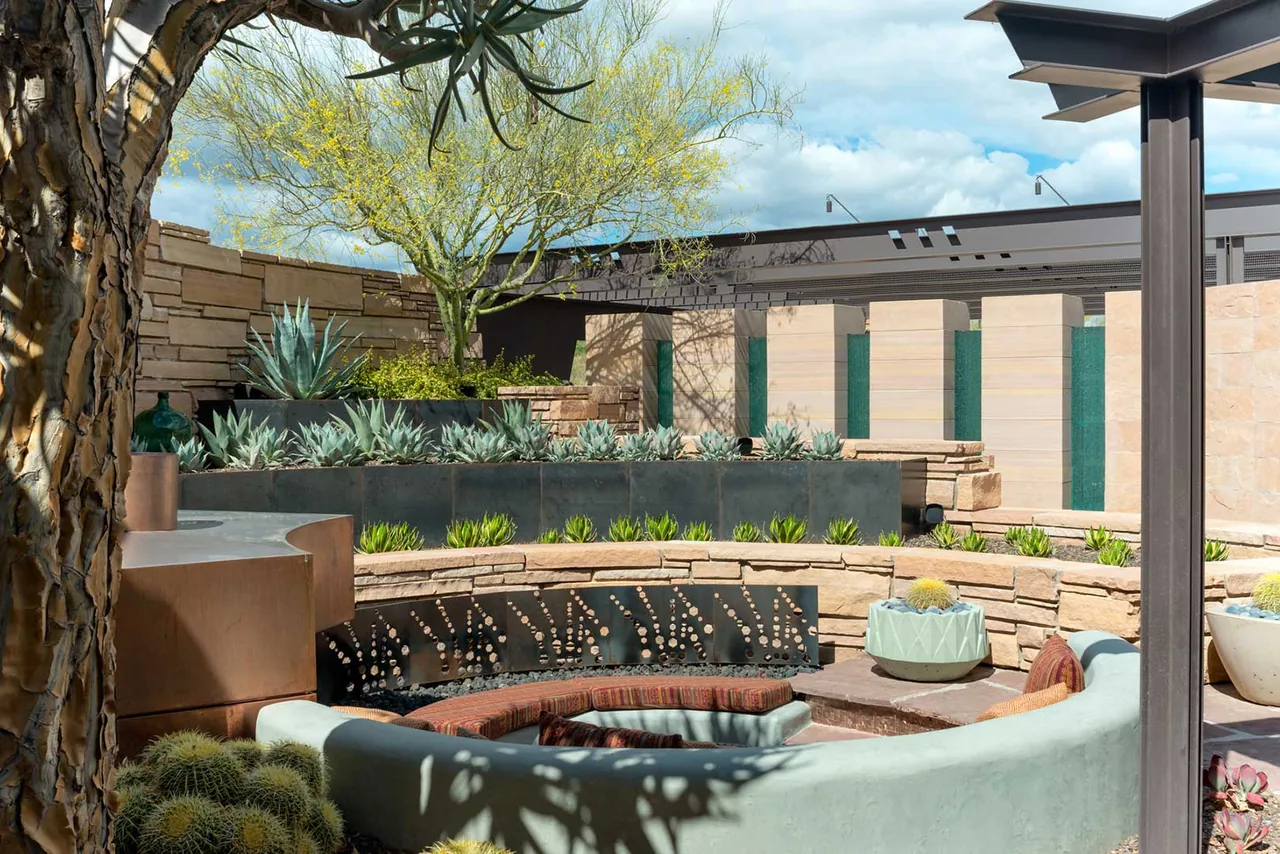 Outdoor courtyard with curving bench seating, desert plants, and stone and metal detailing at Saguaro Ridge project.