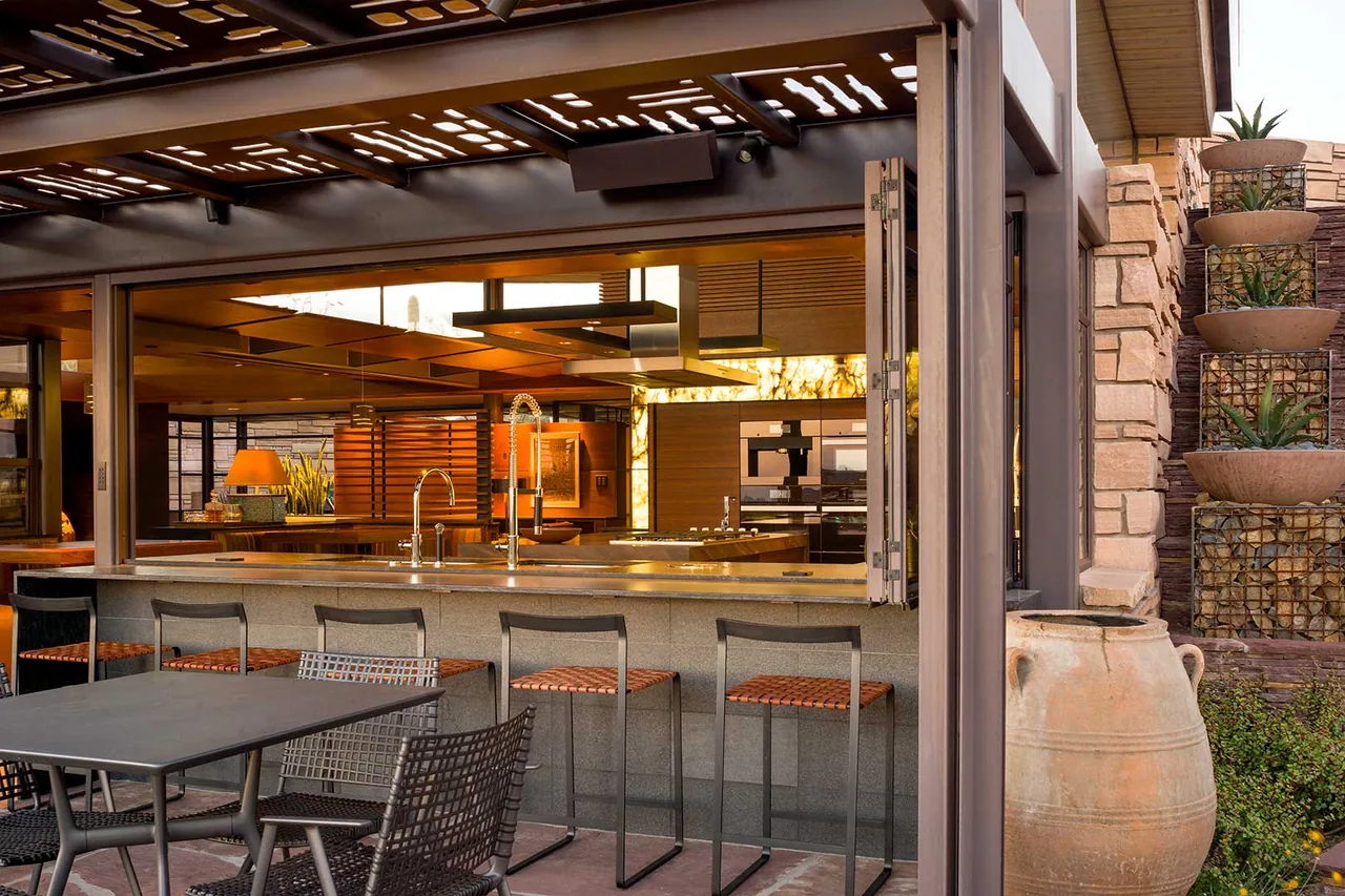 Outdoor bar seating with metal stools faces an open kitchen through large folding windows at Saguaro Ridge.
