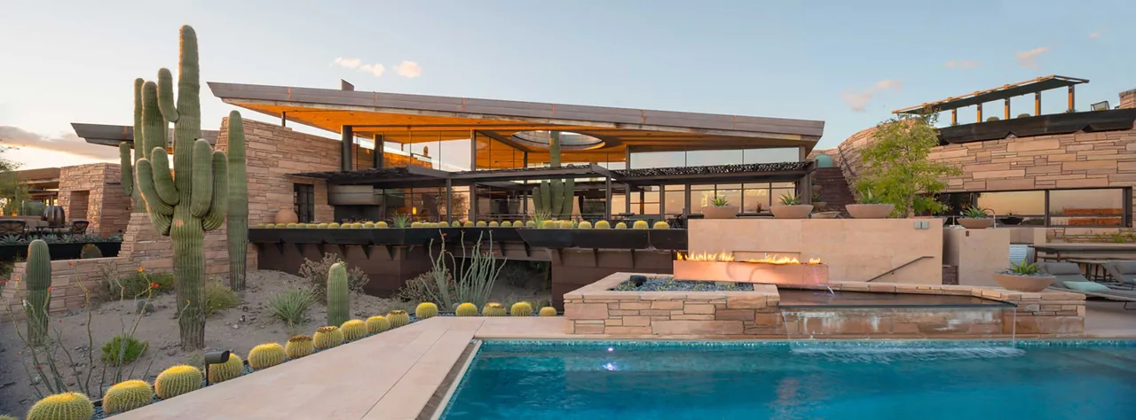 Saguaro Ridge features stone-clad walls, metal pergolas, desert landscaping, and a pool with waterfall at sunset.