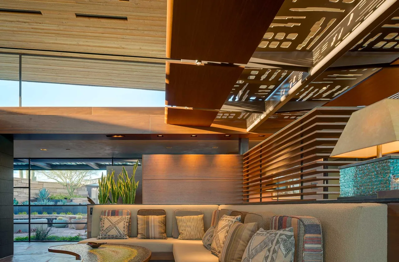 Living room in Saguaro Ridge with wood slat partition, sectional sofa, and desert view through large windows.