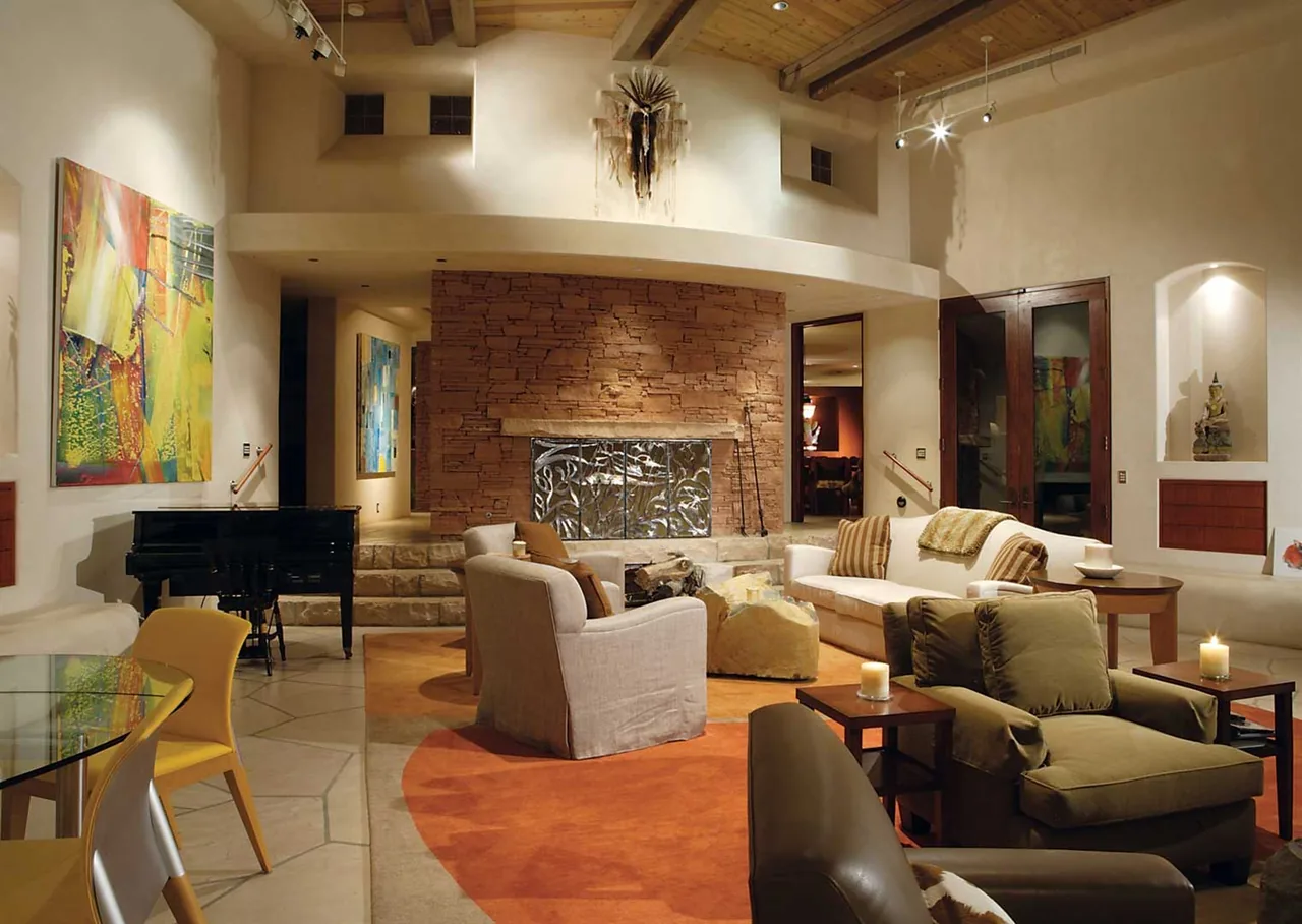Living room in El Rojo Grande features an arched wood ceiling and a red stacked stone fireplace wall with decorative metal screen.
