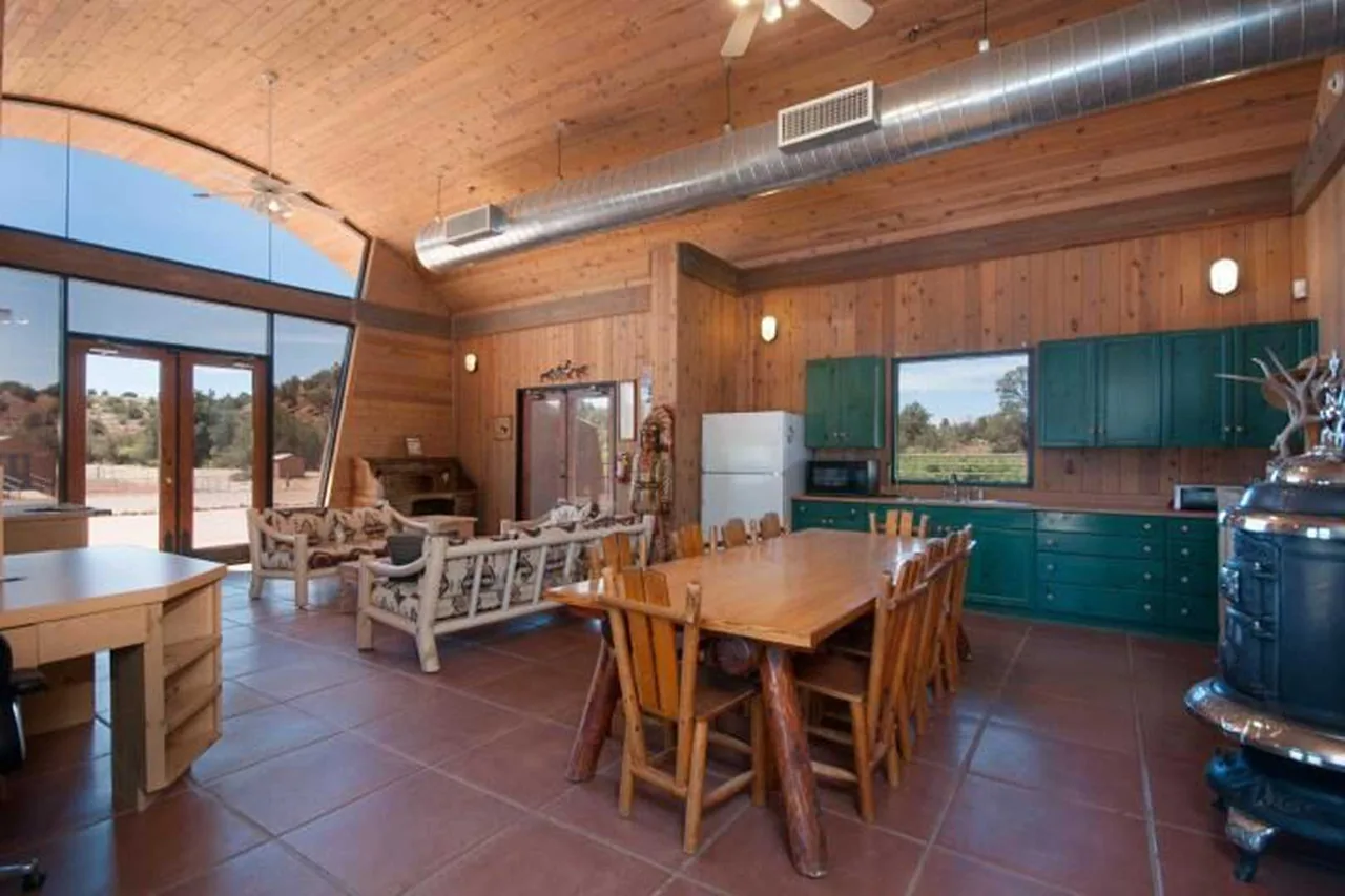 Open kitchen and dining space in a wood-paneled home with green cabinetry and large arched glazing overlooking a desert landscape.