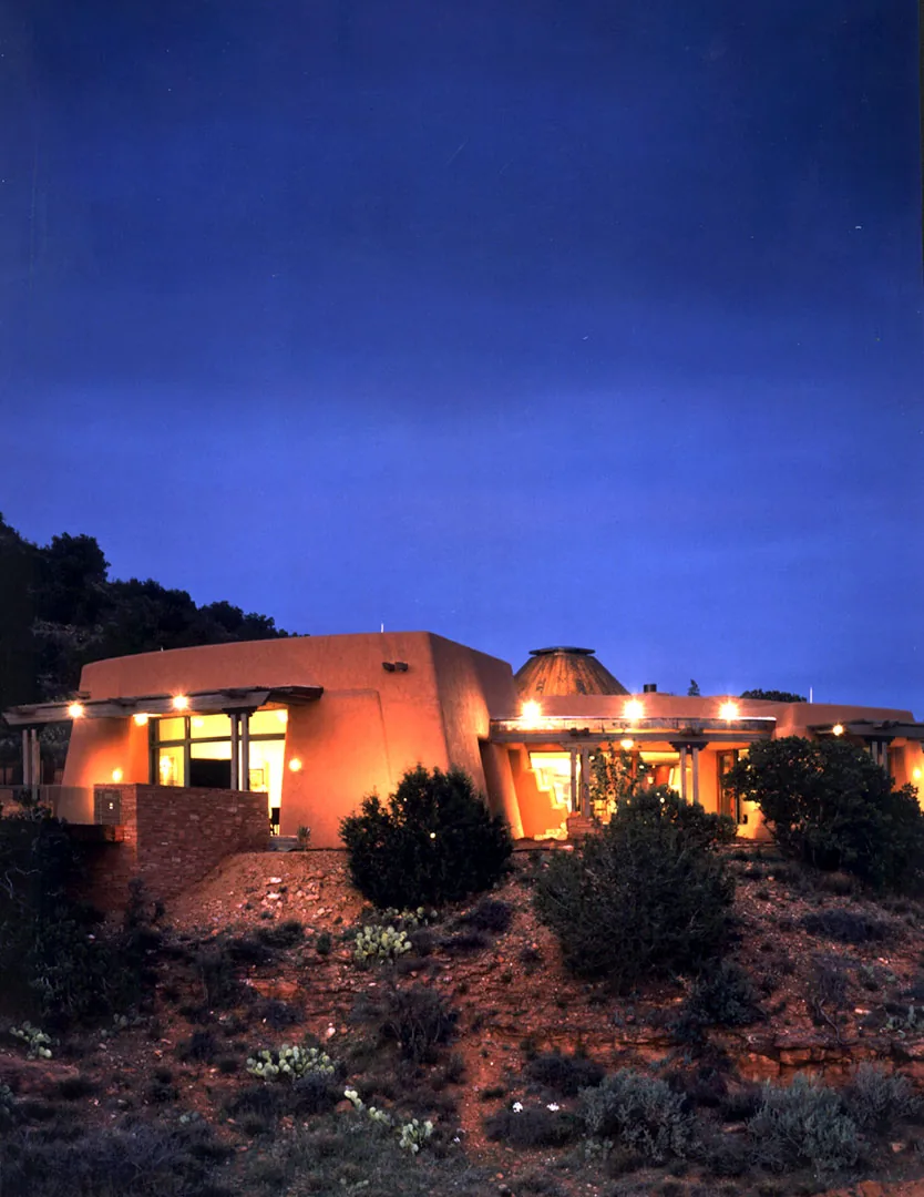 El Rojo Grande project features adobe walls and stone seating illuminated at twilight on a rocky hillside.
