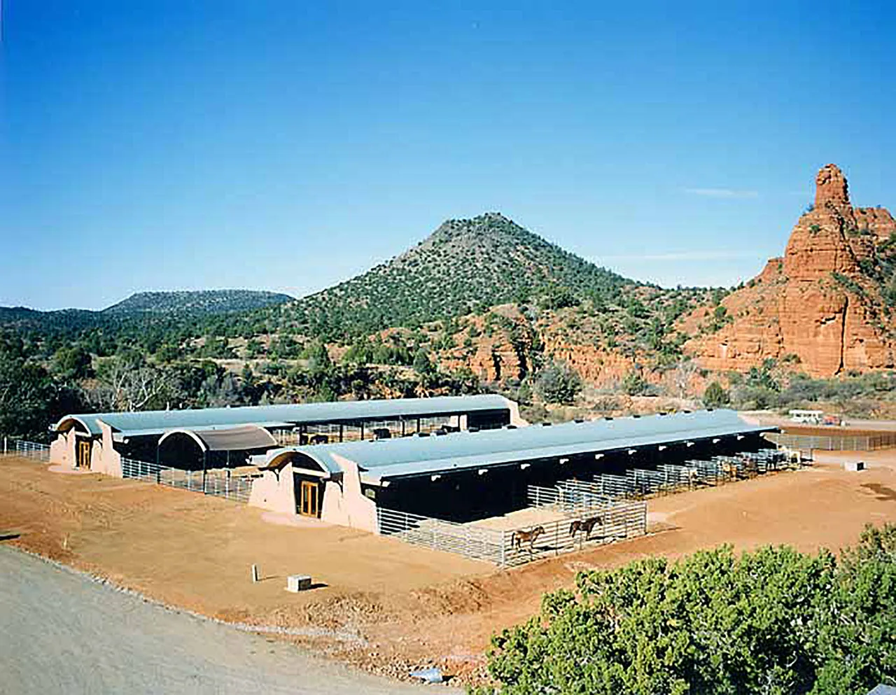El Rojo Grande features two barns with arched metal roofs and adobe walls, set against a rocky desert hillside.
