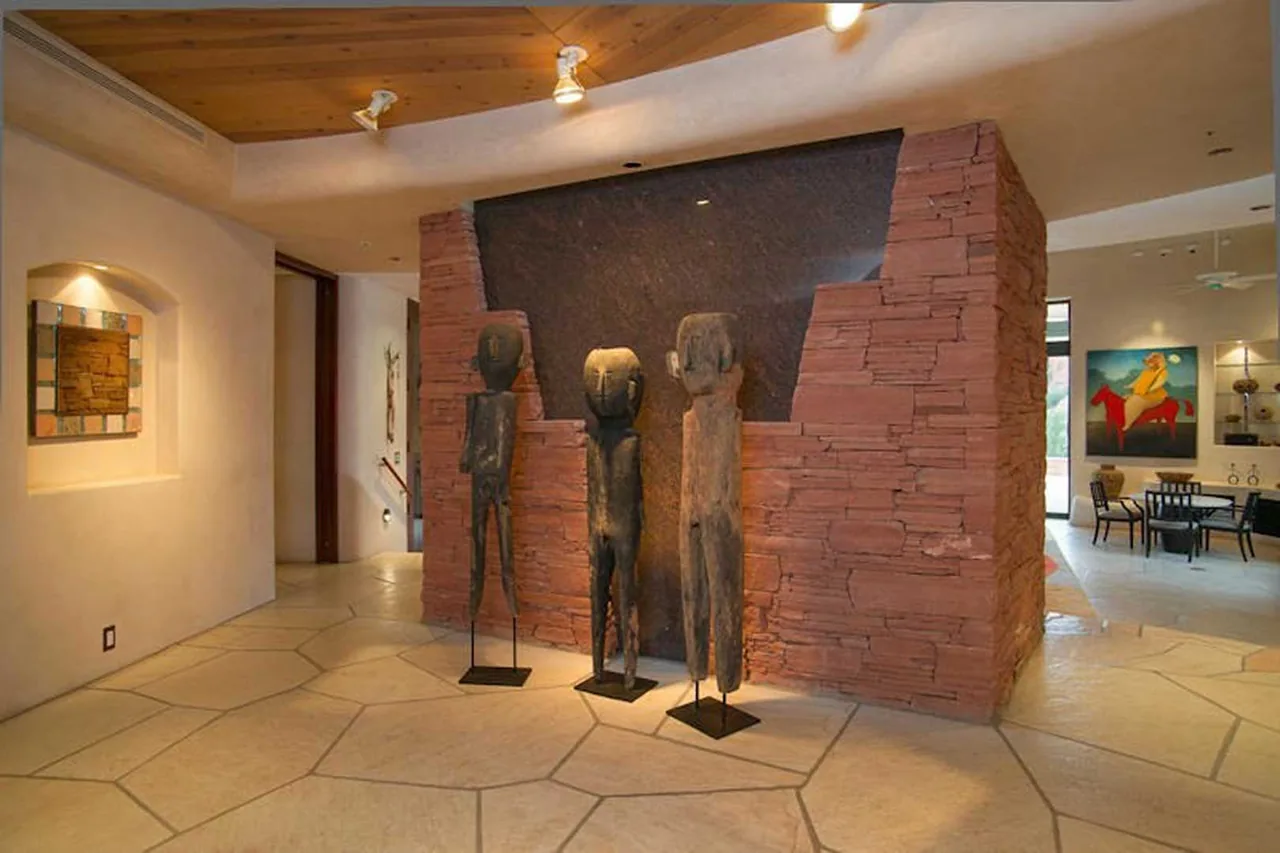 Room features three tall wooden sculptures and a red stacked stone wall with a black inset panel at El Rojo Grande.
