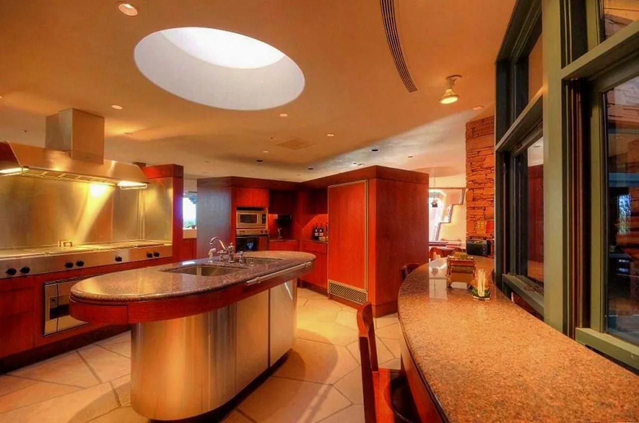Kitchen features a curved island with stainless steel and granite countertop, wood cabinetry, and a circular skylight overhead.