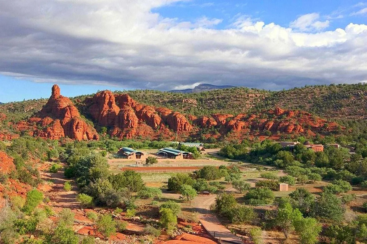 El Rojo Grande project features buildings with arched metal roofs set in a rocky, desert landscape with red rock hillsides.