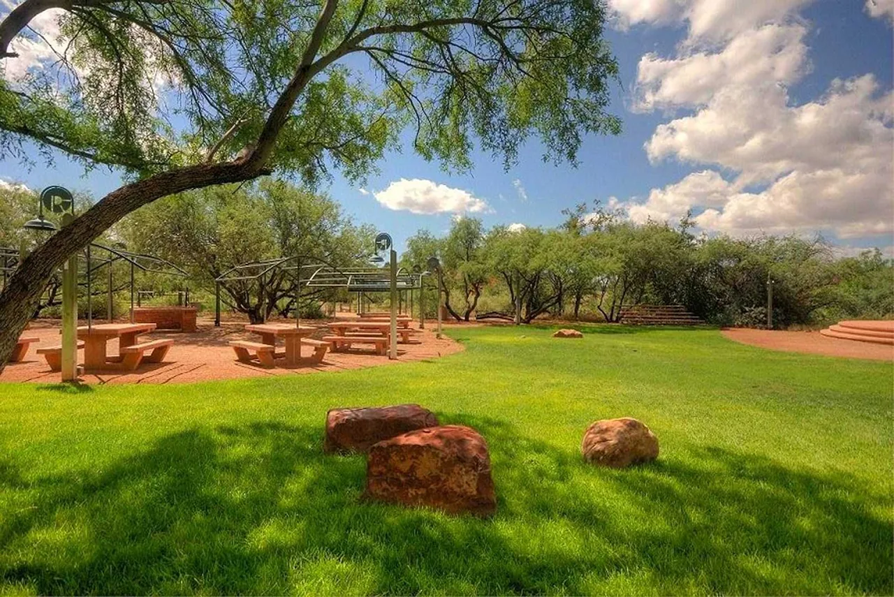 El Rojo Grande features picnic tables under metal pergolas and desert landscaping with rocky hills and green lawn areas.